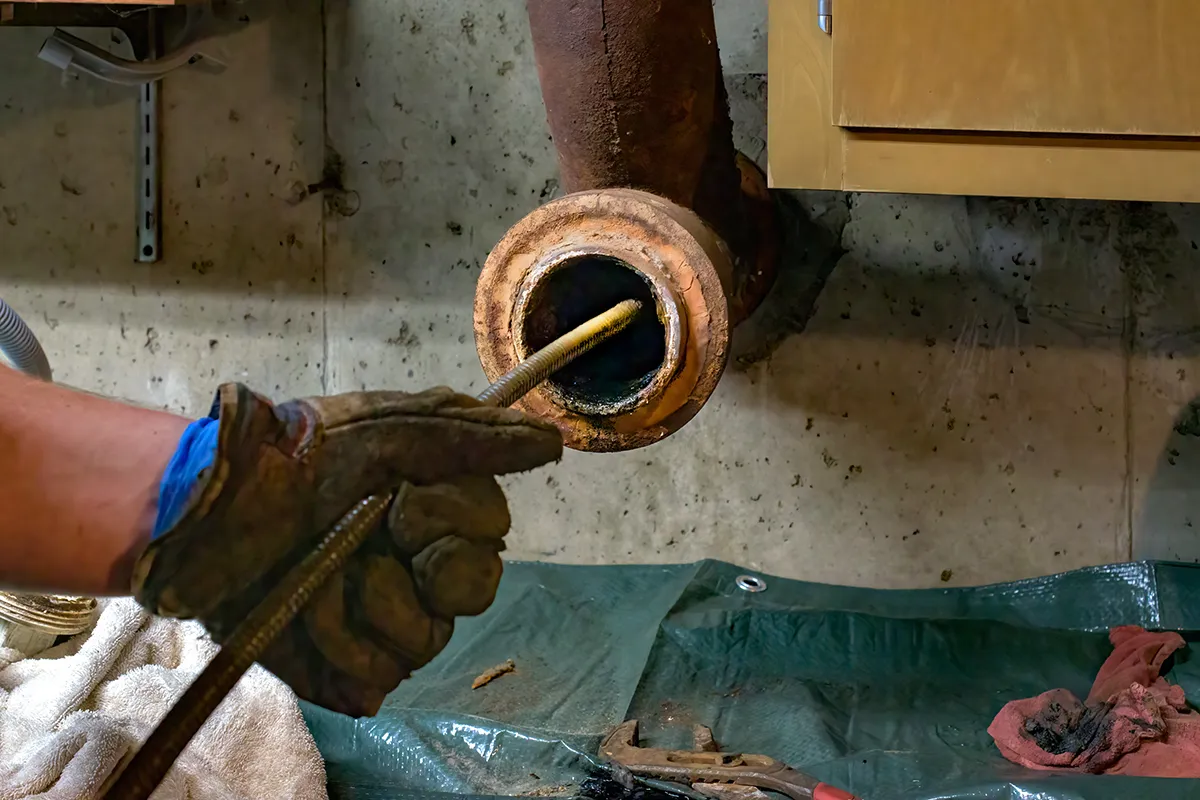 Plumber using a drain snake during drain cleaning service Crowders NC to clear a clogged pipe.